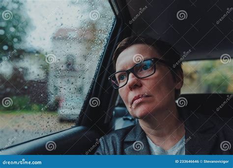 worried businesswoman with eyeglasses waiting in the car and looking out the window during rain