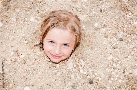 Little Girl Buried In The Sand Of The Beach Stock Photo And Royalty