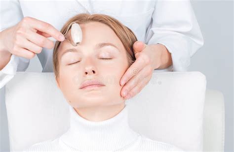 Beautiful Woman Having Face Treatment Cosmetologist Massaging Forehead With Jade Rollers Stock