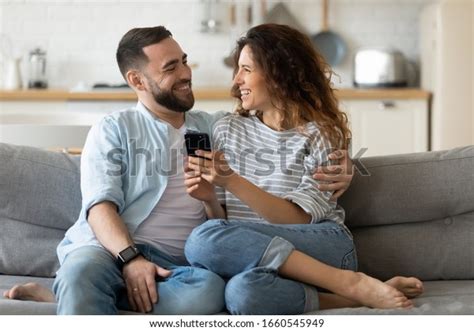 smiling millennial couple sit on couch in kitchen have fun browsing internet on modern