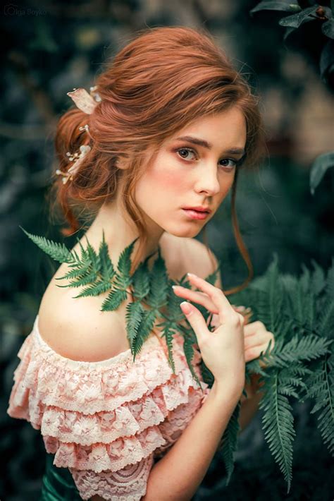 A Woman With Red Hair Wearing A Pink Dress And Holding Green Leaves In