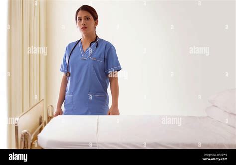 Portrait Of A Young Nurse Standing Beside Patient Bed In Hospital Ward