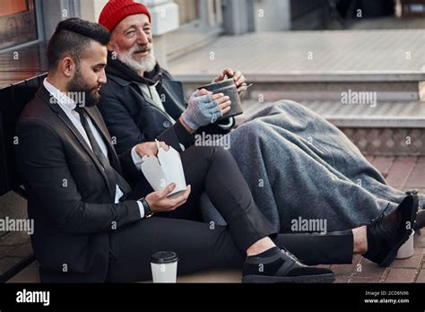 Handsome Businessman In Suit Sitting On Floor With Homeless Man