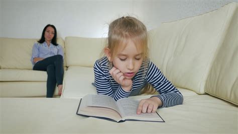 Mother And Daughter Reading Book Sitting On Sofa At Home Stock Video