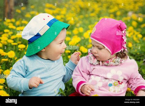 Little Boy And Girl In Hats Sitting On The Field With Soft Toys In