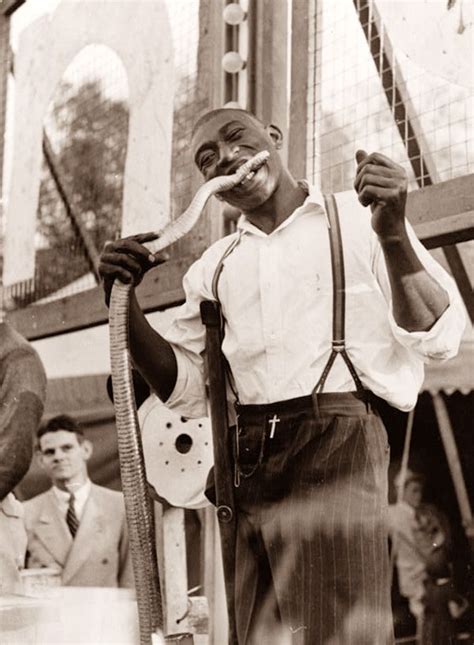 A Black And White Photo Of A Man Holding A Large Snake In His Right Hand