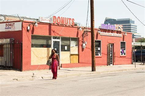 A Woman Is Walking Down The Street In Front Of A Donut Shop That Has