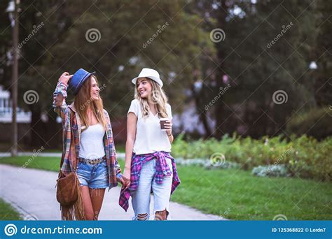 Two Young Women Holding Hands Walking In Green Park Best Friends Stock