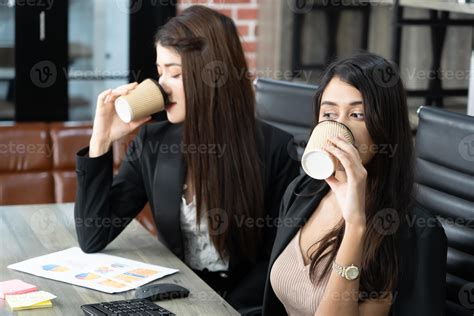 Office Coffee Break With Two Female Colleagues Sitting Chatting Over Cups Of Coffee Asian