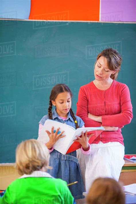 Primary Schoolgirl Reading Book At Front Of Classroom Stock Photo