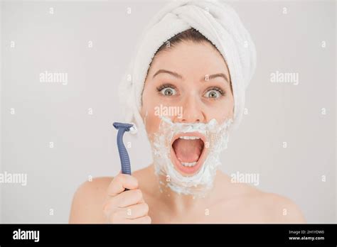 funny portrait of a woman with shaving foam on her face holding a razor on a white background