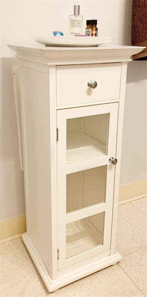 Provide a sophisticated space for your bathroom accessories by bringing in this transitional style bathroom cabinet, featuring spacious storage with 1 drawer and 2 doors which open to reveal an adjustable shelf. White Wood Bathroom Storage Stand-alone with Glass Cabinet ...