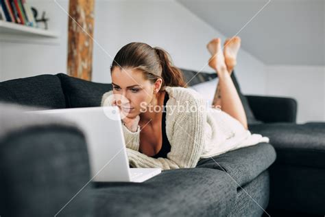 Portrait Of Young Woman Working On Laptop While Lying On Sofa Female Using Laptop At Home