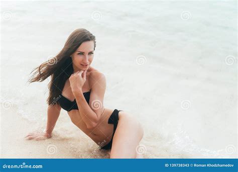 Tanned Girl In Black Swimsuit Posing On Sandy Beach Near Ocean Beautiful Model Sunbathes And