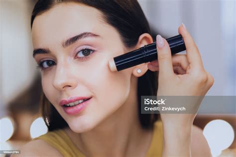 Charming Woman Using Concealer Stick While Putting Makeup On Stock