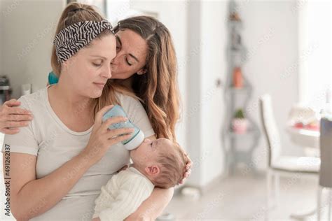 A Lesbian Couple Giving A Bottle Of Milk To Their Baby Kissing Each