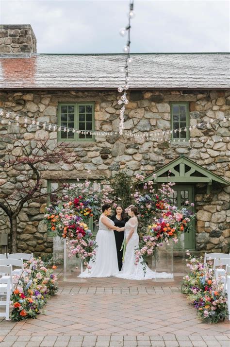 A Bride And Groom Standing In Front Of A Stone Building With Flowers On