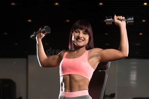 Woman Exercising Shoulders With Dumbbells In The Gym And Flexing Stock