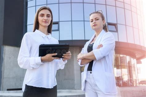 Two Business Women With Tablets Standing Outside Business Building