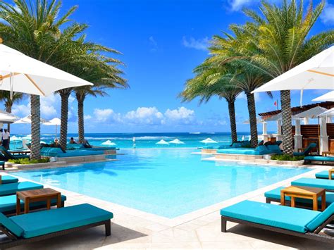 An Outdoor Pool With Chaise Lounges And Umbrellas Next To The Ocean On