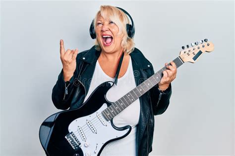 Middle Age Blonde Woman Playing Electric Guitar Doing Horns Sign With