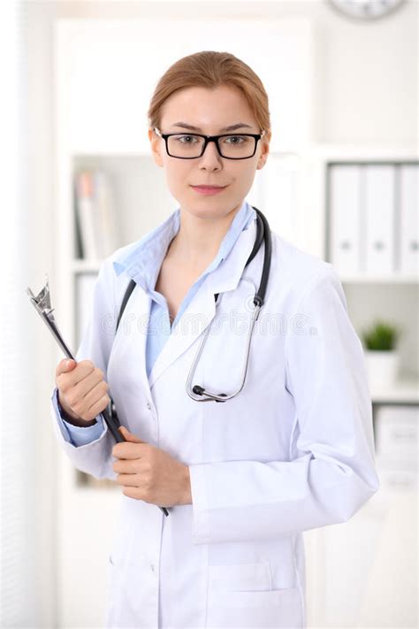 Young Brunette Female Doctor Standing With Clipboard Near Window In