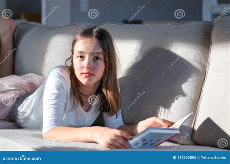 hard light portrait of cute tween girl lying on sofa with book looking at camera with funny