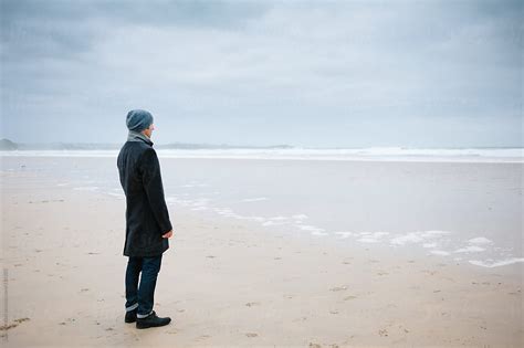 Man Standing Alone On The Beach Looking Out To Sea By Stocksy