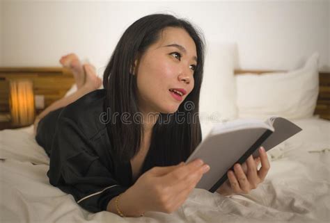 Young Beautiful And Sweet Asian Chinese Woman In Bed Reading Book Novel Feeling Happy And