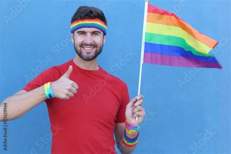 Handsome Gay Man Showing Handlikethumb Up Holding Rainbow Gay Flag Isolated On Blue Background