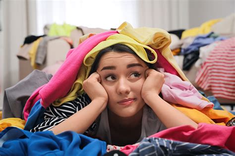 Pensive Young Woman With Lots Of Clothes On Floor In Room Fast Fashion
