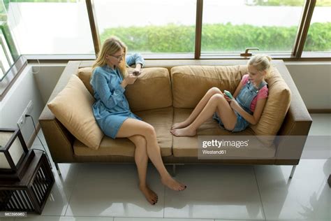 Mother And Daughter Sitting In Modern Living Room On A Couch Using