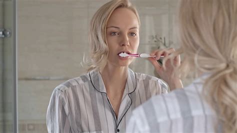 Blonde Woman Brushing Teeth In Front Of The Mirror In Bathroom Stock