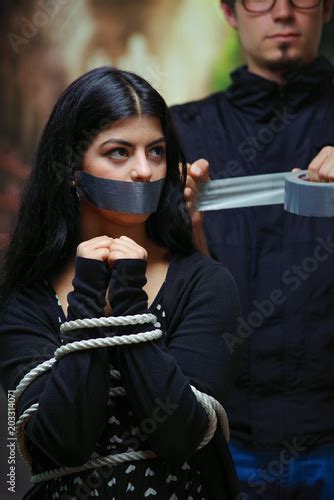 Close Up Of A Mans Covering A Womans Mouth With Tape Tied With Rope
