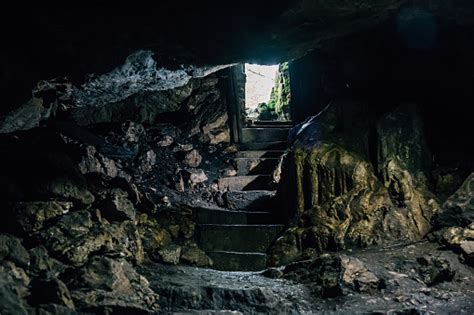 Dark Cave With Steps Of Staircase And Light From Entrance Stock Photo