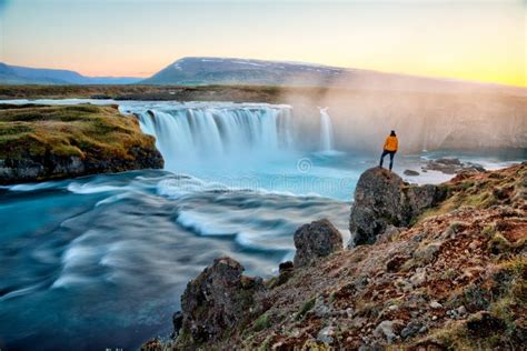 Man Standing By Amazing Godafoss Waterfall In Iceland During Sunset