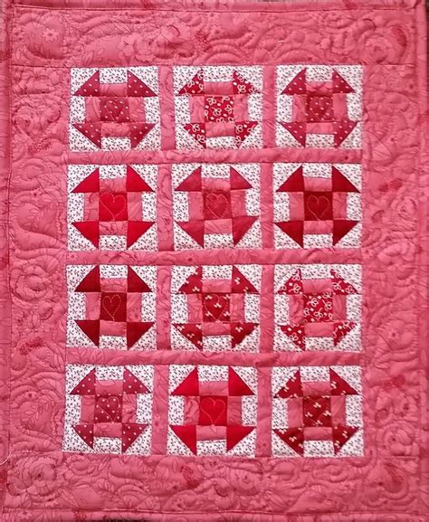 A Pink Quilted Wall Hanging With Red And White Squares In The Shape Of