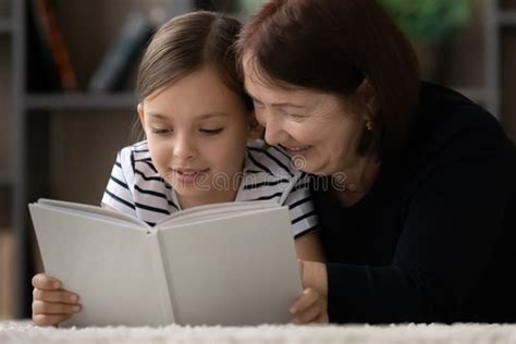 Smiling Mature Grandmother With Little Girl Reading Book Together Stock
