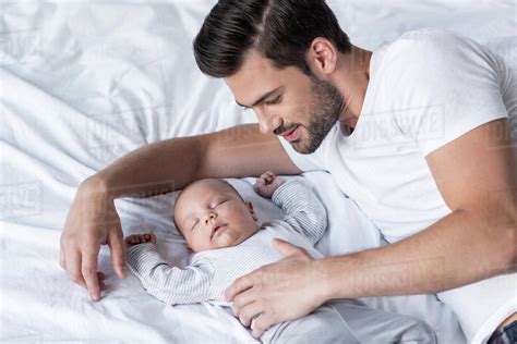 Handsome Father Lying On Bed With Sleeping Baby Boy Stock Photo