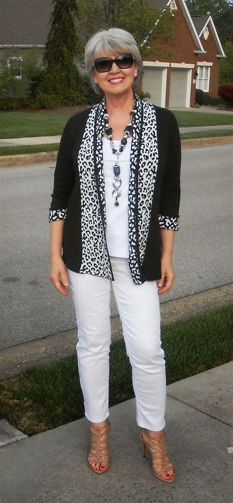 a woman standing on the sidewalk wearing white pants and a black cardigan sweater with leopard print