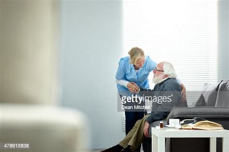 Female Caregiver Helping Senior Man Get Up From Couch High Res Stock