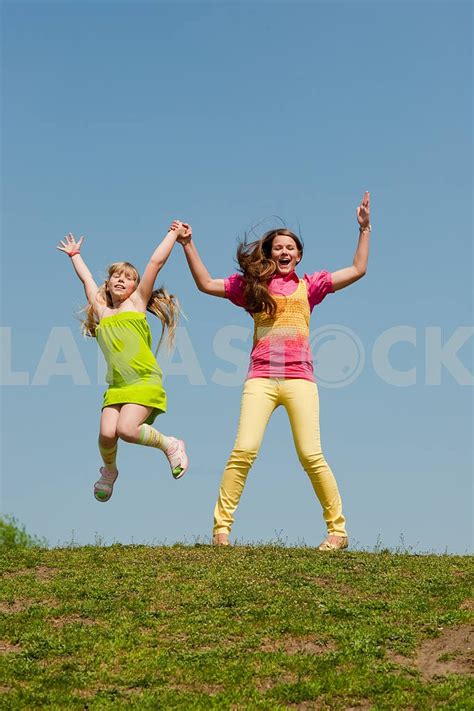 Two Girls Jumping On Green Meadow Eduard Stelmakh Larastock