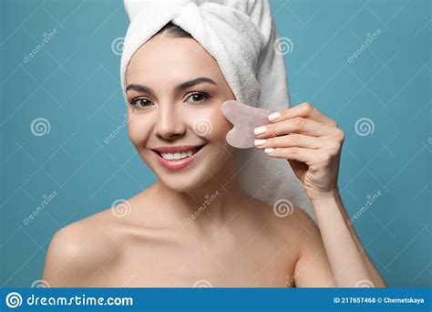 Belle Jeune Femme Faisant Le Massage Du Visage Avec Loutil Gua Sha Sur Fond Bleu Photo Stock