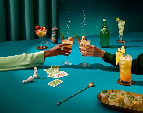 two people toasting with cocktails and playing cards on the table next to them