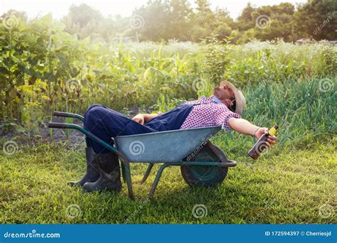 Young Male Farmer Is Relaxing In Wheelbarrow On The Green Garden