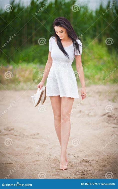 Привлекательная девушка брюнет с коротким белым платьем гуляя Barefoot на дороге сельской