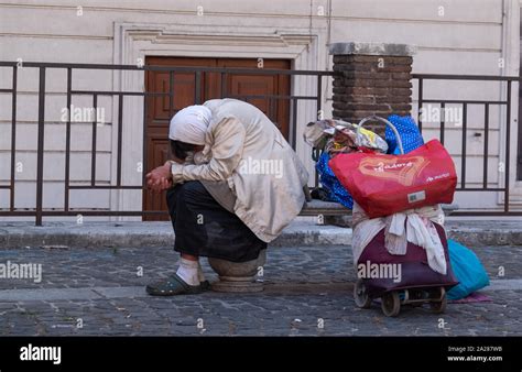 seated homeless woman with bowed covered head with all her belongings on a trolley behind her in