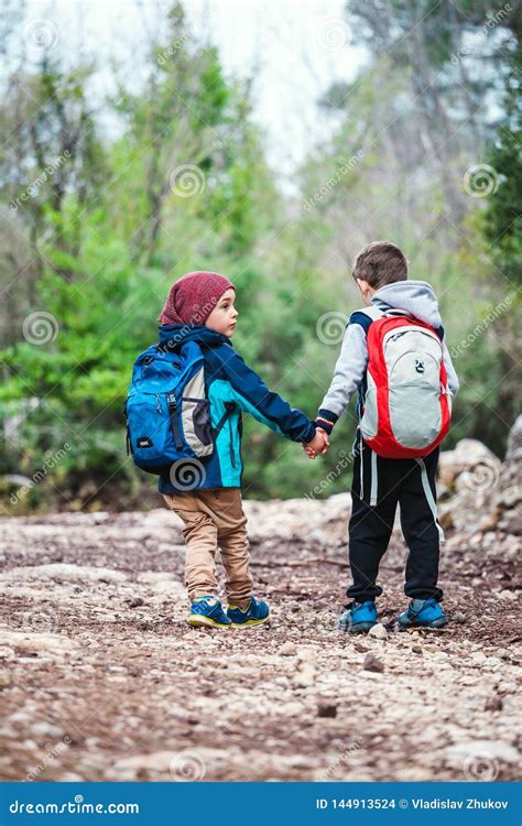 Two Boys With Backpacks Are Walking Along A Forest Path Stock Photo