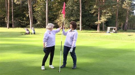 Two Women In White Shirts Holding Red Flags On A Golf Course