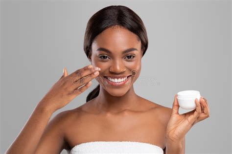 Glad Young Black Woman With Perfect Skin Applying Moisturizing Anti Aging Cream On Her Face And